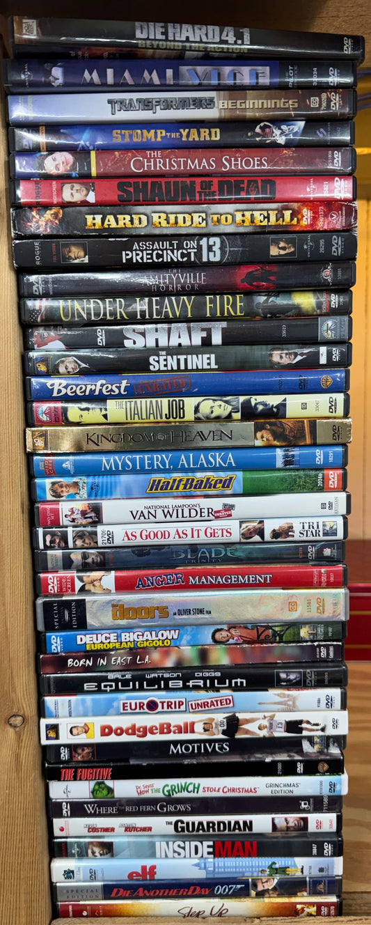 A row of assorted DVD movie cases standing upright on a wooden shelf, with many titles visible including titles like The Godfather, The Simpsons, Batman, and Spider-Man.