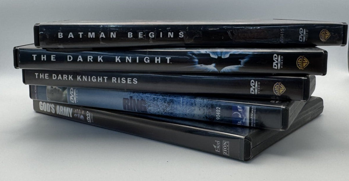 A stack of five Batman-themed DVD cases, including Batman Begins, The Dark Knight, The Dark Knight Rises, and The Dark Knight: Death of the Knight, displayed on a white surface between two textured gray side panels.