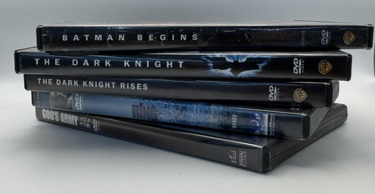 A stack of five Batman-themed DVD cases, including Batman Begins, The Dark Knight, The Dark Knight Rises, and The Dark Knight: Death of the Knight, displayed on a white surface between two textured gray side panels.